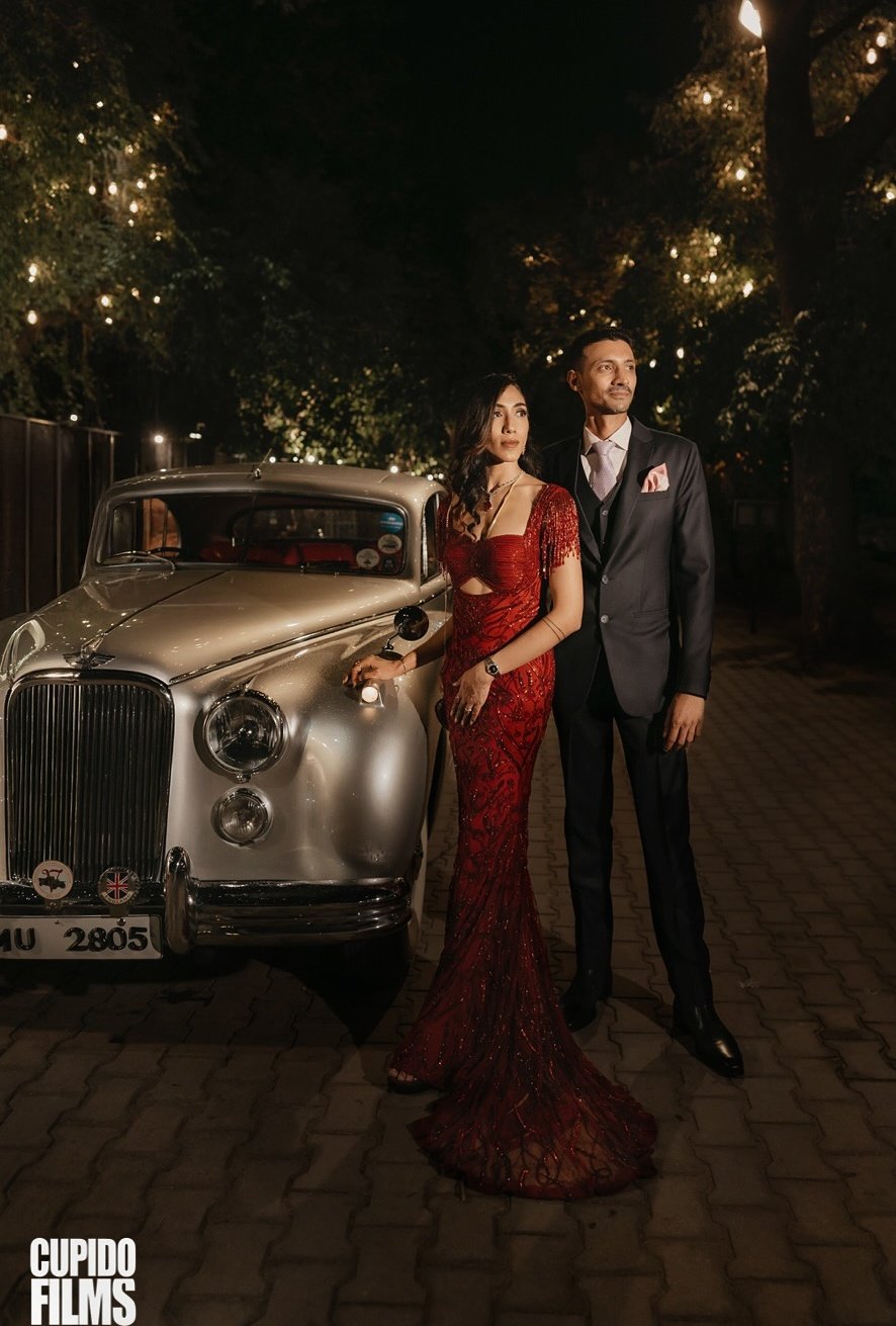 A wedding couple posing beside a vintage car at night